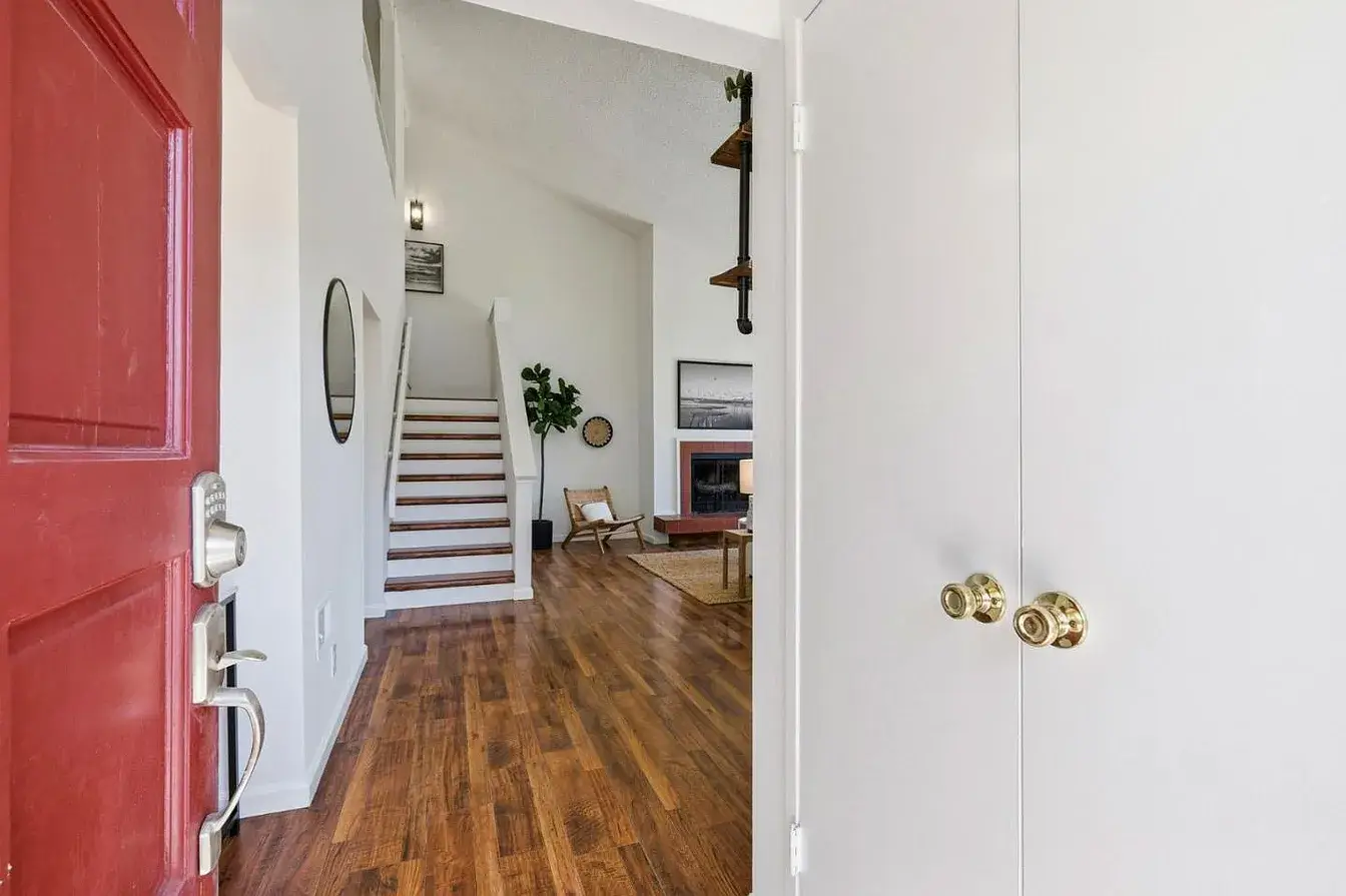 Santa Cruz Home Entry View With Open Staircase and Wood Floors Interior entry view of a Santa Cruz home with a red front door, warm wood floors, white walls, an open staircase, and a staged living area with a fireplace in the background. This Santa Cruz property image highlights a bright entryway, clean interior presentation, and an open layout that can appeal to buyers comparing homes for sale in Santa Cruz County.