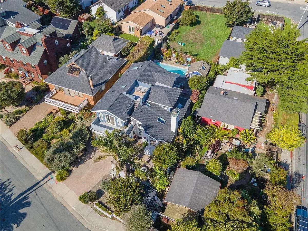 Aerial view of a Santa Cruz property showing the main home, surrounding landscaping, neighboring homes, multiple outbuildings, and a large backyard lot near a residential street. This Santa Cruz home image highlights lot size, neighborhood context, and outdoor space, which are important features for buyers comparing Santa Cruz properties and homes for sale in Santa Cruz County.
