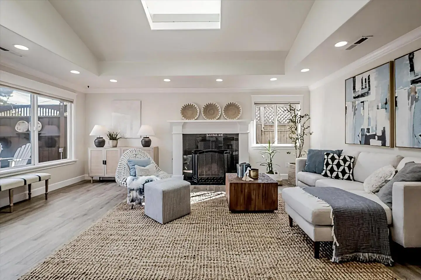Staged Santa Cruz Living Room With Fireplace and Natural Light Bright and airy staged living room in a Santa Cruz home featuring a modern fireplace, woven rug, comfortable sofa with decorative pillows, accent chair with ottoman, wooden coffee table, indoor plants, large windows letting in natural light, and neutral tones that highlight the contemporary design of the property. Ideal for showcasing houses for sale in Santa Cruz.