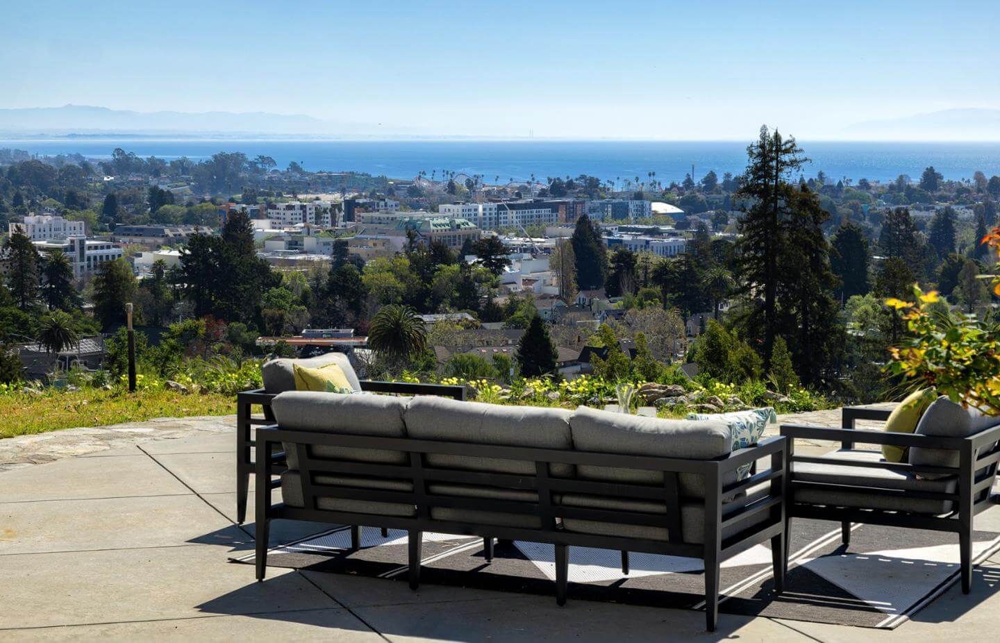 Santa Cruz Ocean View Patio and Coastal Home Value Outdoor patio seating area overlooking Santa Cruz neighborhoods, trees, downtown buildings, and the coastline in the distance. This image highlights how ocean views, usable outdoor space, natural light, and coastal location can influence buyer interest and home value for Santa Cruz properties.