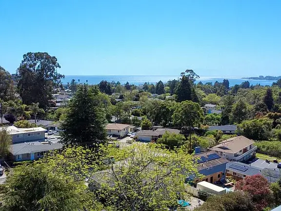 Aptos California Neighborhood With Coastal Ocean View Aerial view of a residential neighborhood in Aptos, California, with single-family homes, mature trees, landscaped yards, and a view of the Pacific Ocean in the distance, highlighting the coastal setting of Santa Cruz County real estate.