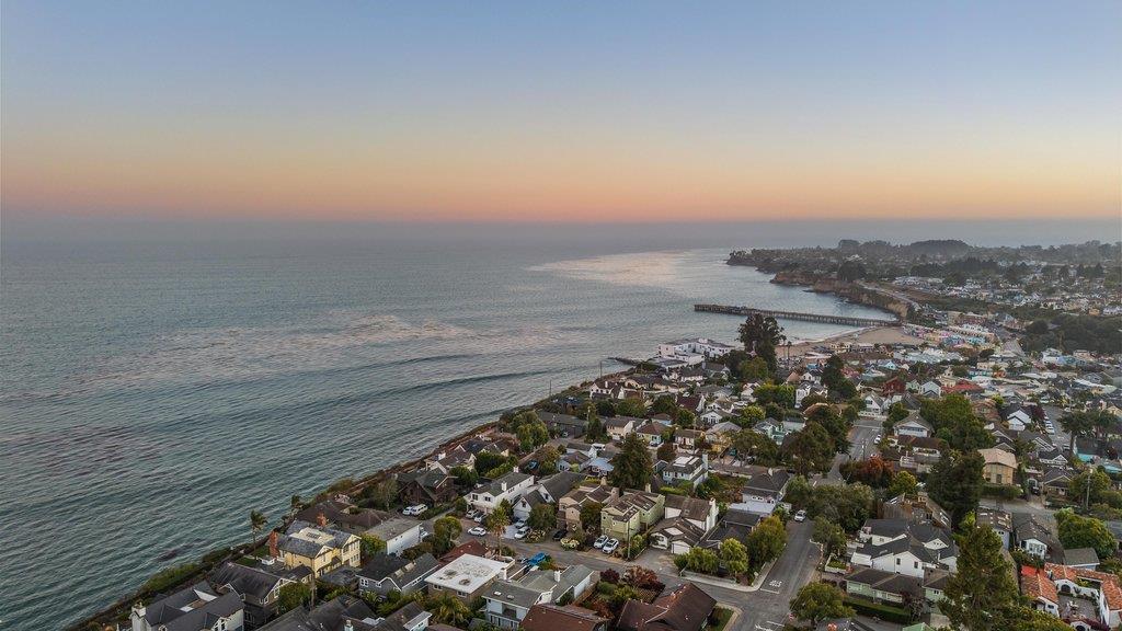 Aerial view of Capitola in Santa Cruz County showing coastal residential homes, neighborhood streets, the shoreline, and Monterey Bay at sunset, highlighting the close connection between Capitola real estate and the coast.