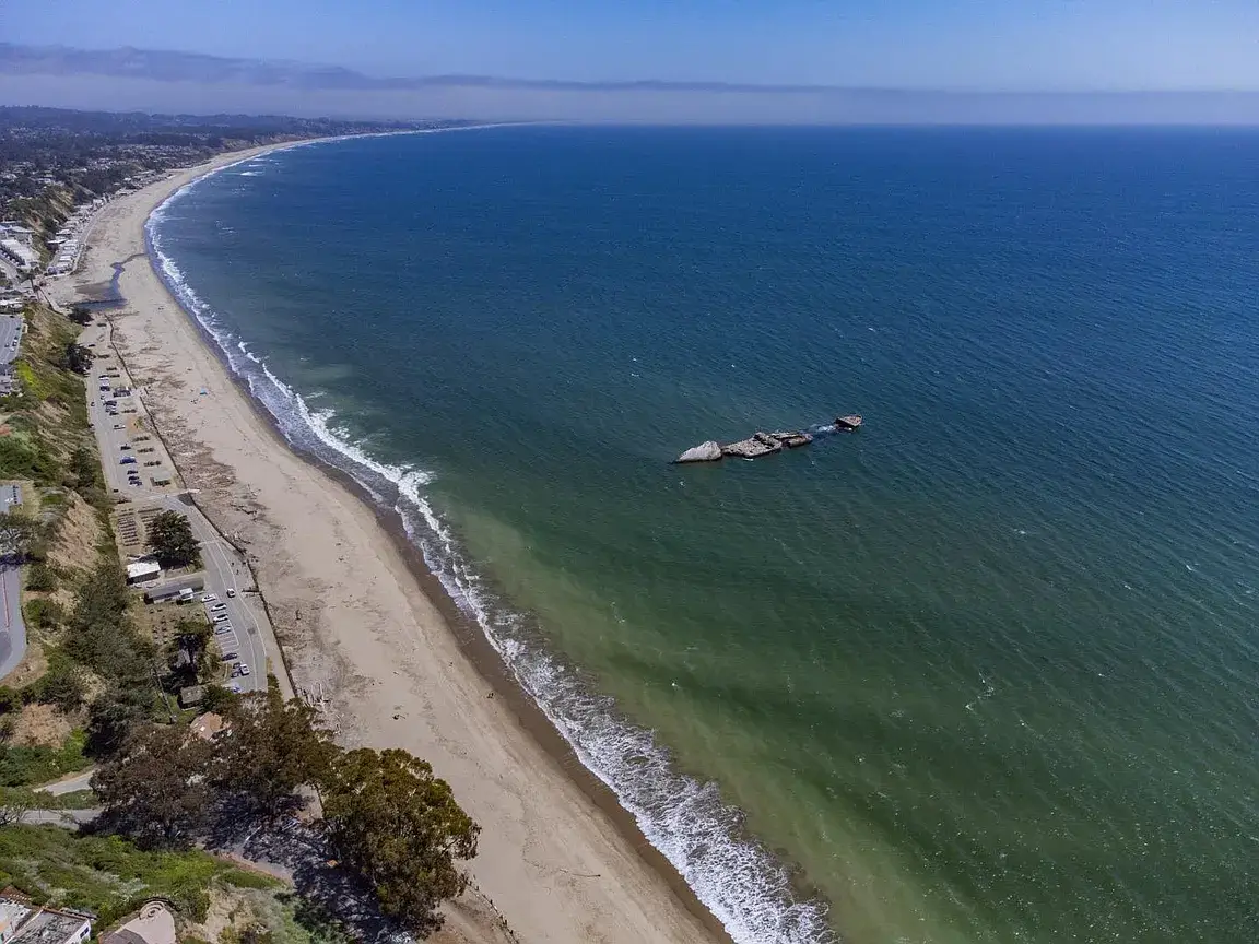 Aptos Coastal Beach and Oceanfront Homes in Santa Cruz County Aerial view of the Aptos coastline in Santa Cruz County, California, showing a wide sandy beach, Pacific Ocean, coastal bluffs, shoreline road, and nearby residential homes.