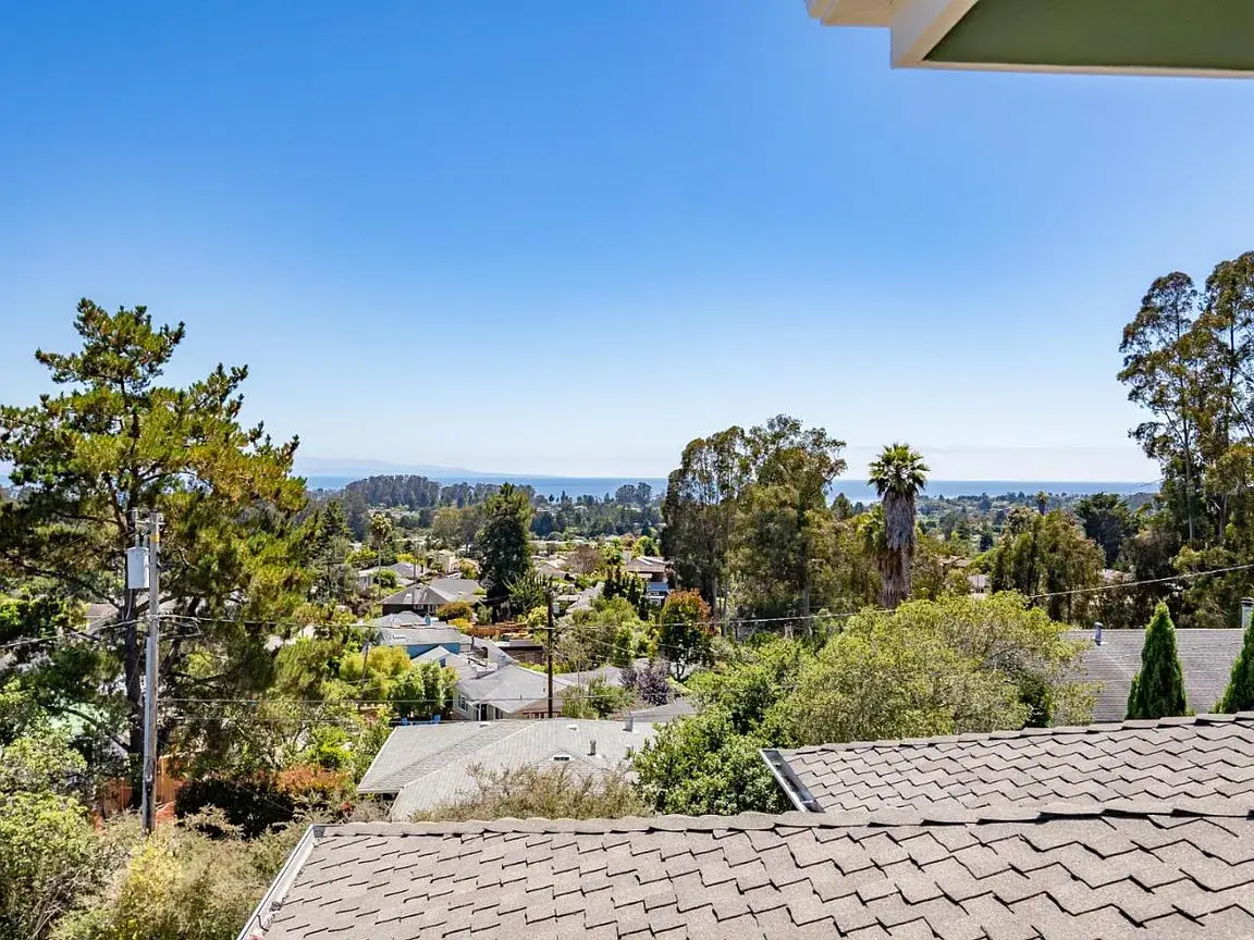 View from a Soquel hillside home overlooking a residential neighborhood with tree-lined streets, single-family homes, mature landscaping, and the Pacific Ocean visible in the distance, highlighting the coastal setting of Santa Cruz County real estate.