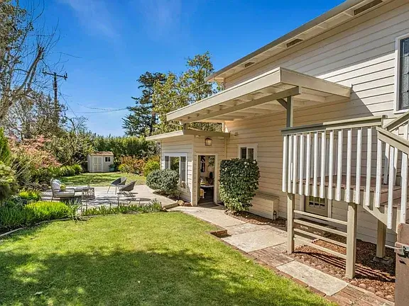 Exterior of a Soquel home with a well-maintained lawn, landscaped yard, covered entry, outdoor seating area, and mature greenery, showcasing residential property features common in Santa Cruz County real estate.